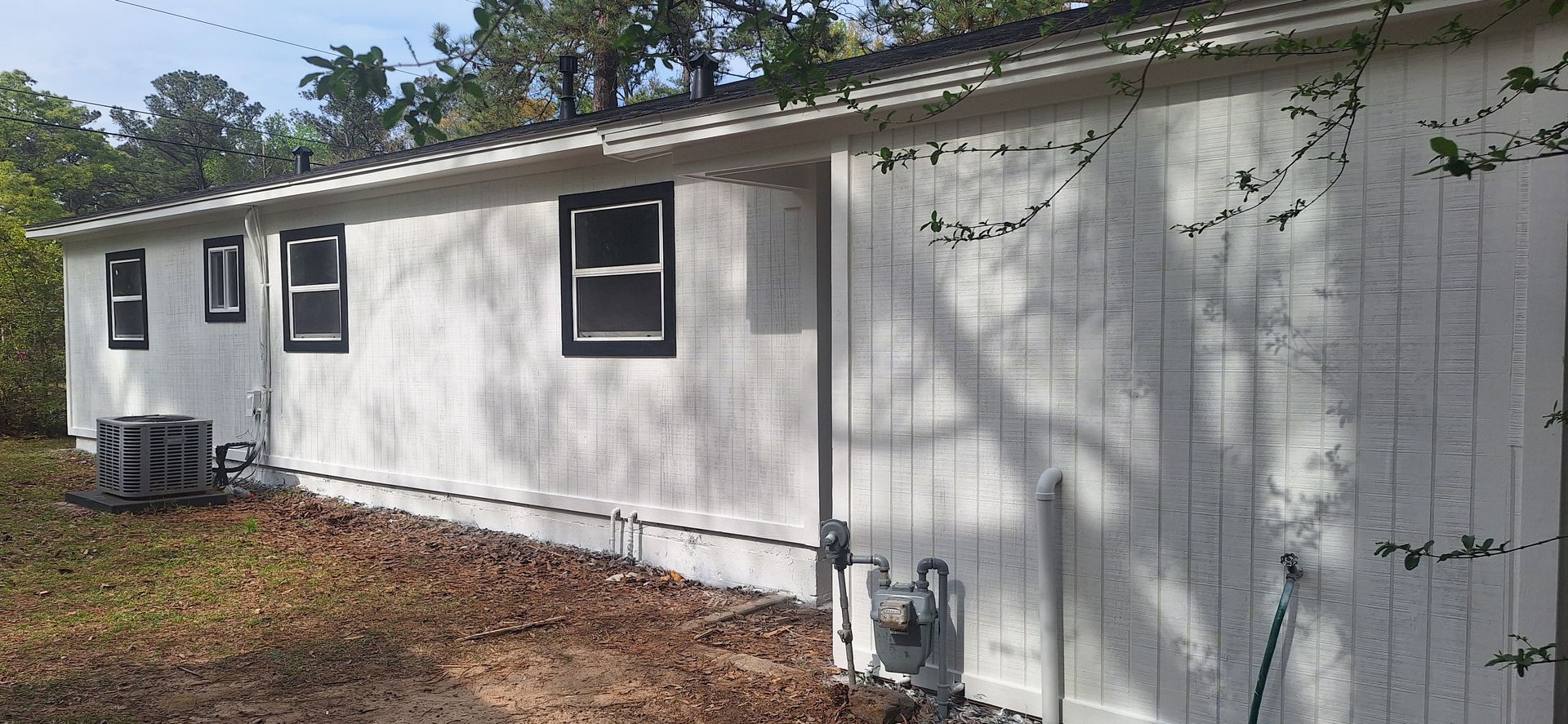 White house exterior with small windows, AC unit, and utility meters along the side