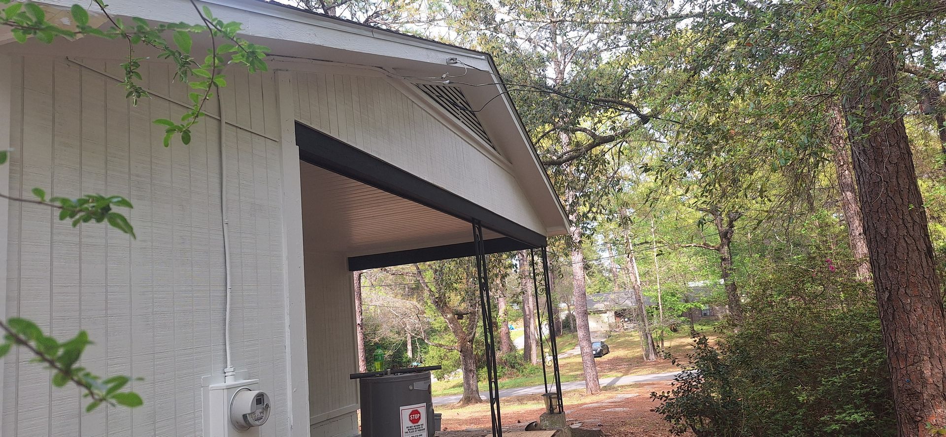 White house corner with covered porch in a wooded yard with trees and dirt path