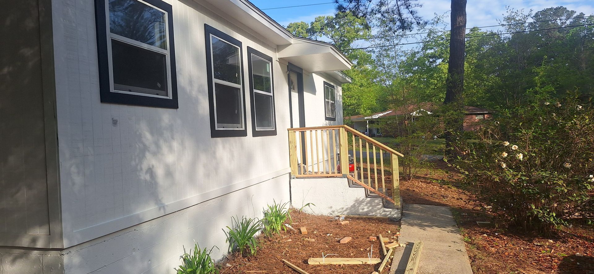 White house exterior with black-trimmed windows, a small porch, and a concrete walkway along the side.