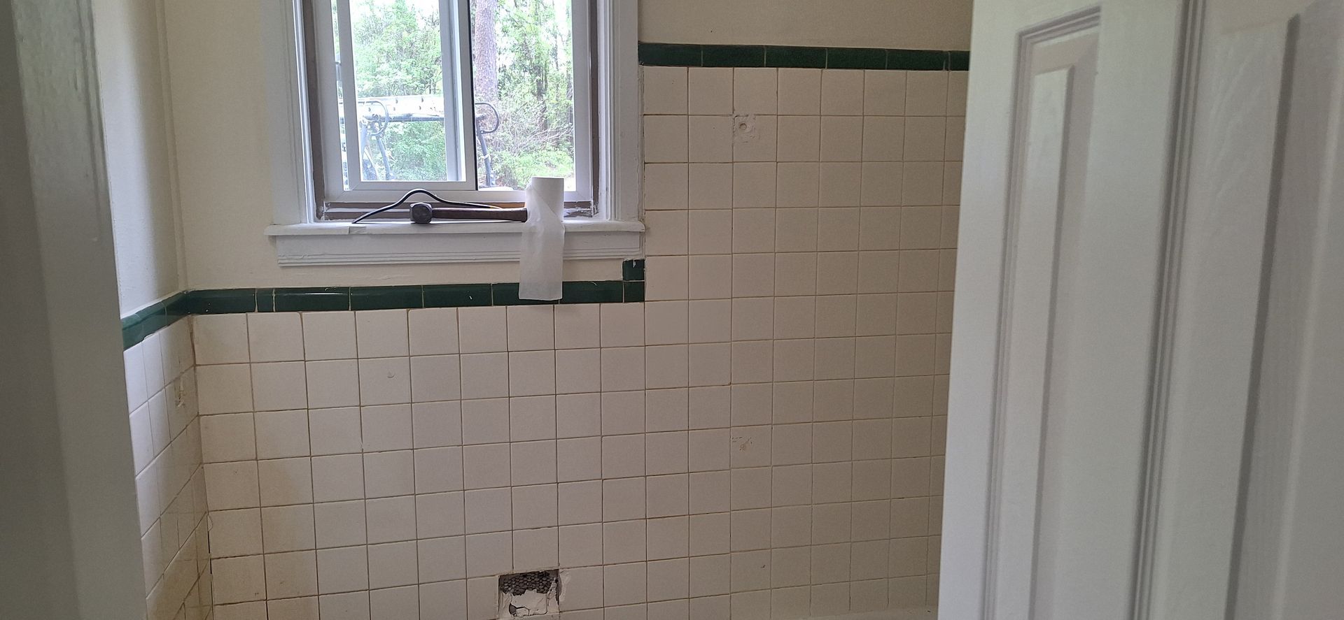 Small bathroom with white tile walls, green trim, and a window above a tub area.