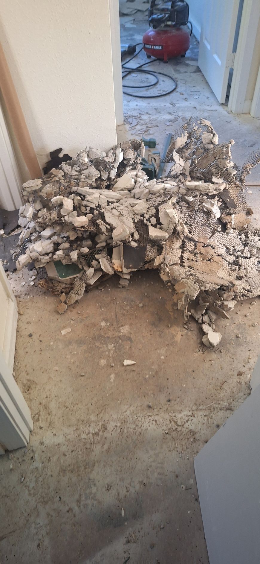 Pile of broken drywall and debris in a hallway doorway on a worn carpet.