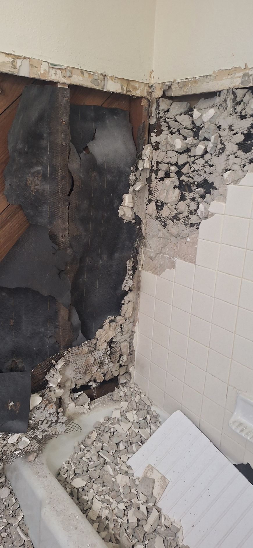 Severely damaged bathroom wall with exposed blackened studs, broken tile, and debris on the floor
