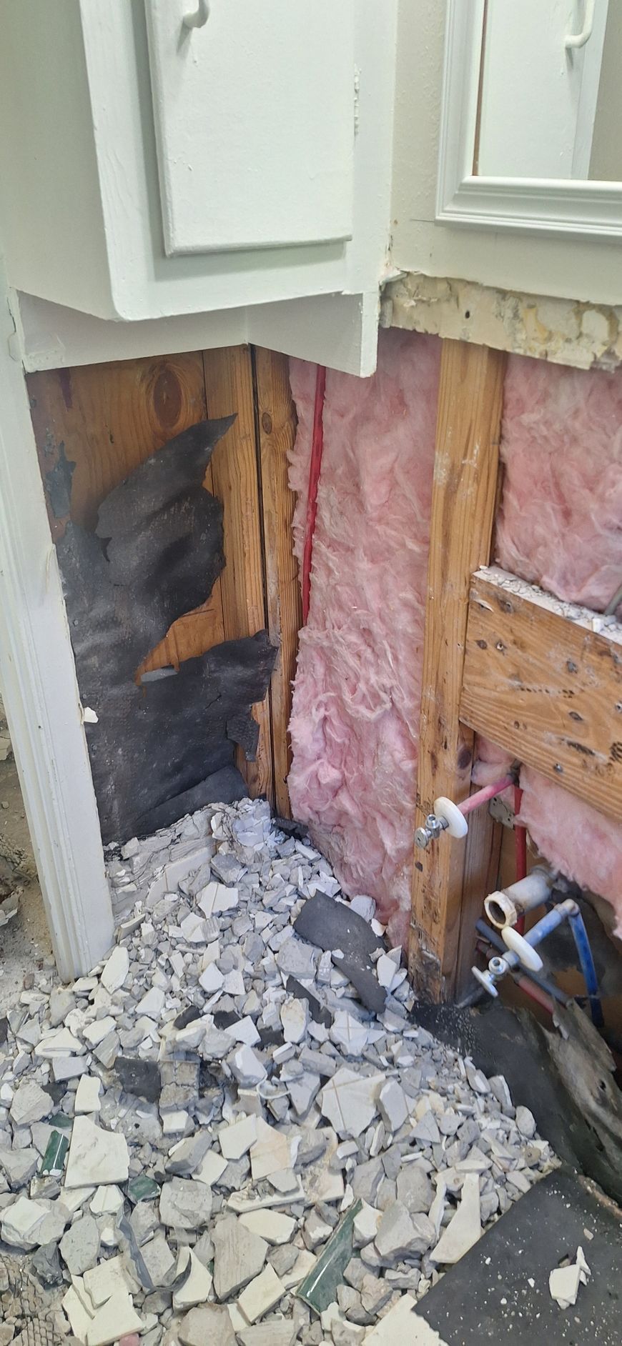 Damaged exterior wall with exposed insulation, broken siding, and debris on the ground