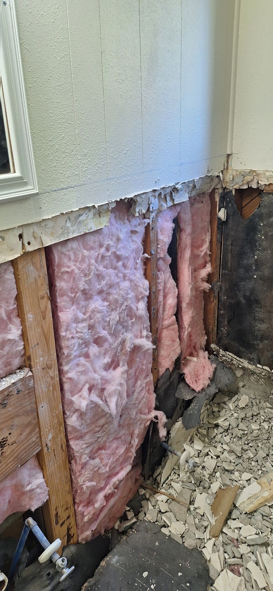 Damaged exterior wall with exposed pink insulation and crumbling siding near the foundation