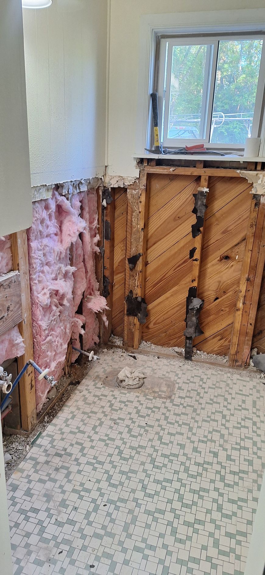 Partially demolished room with exposed pink insulation, wood framing, and a window.