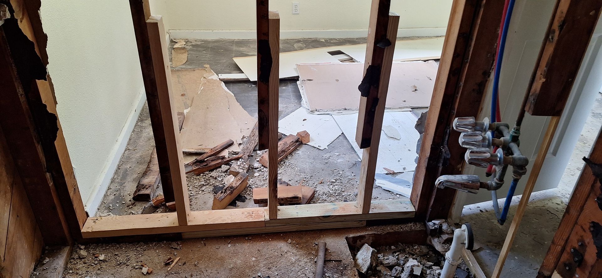 Partially demolished interior wall with exposed framing and debris on the floor, plus pipes on the right