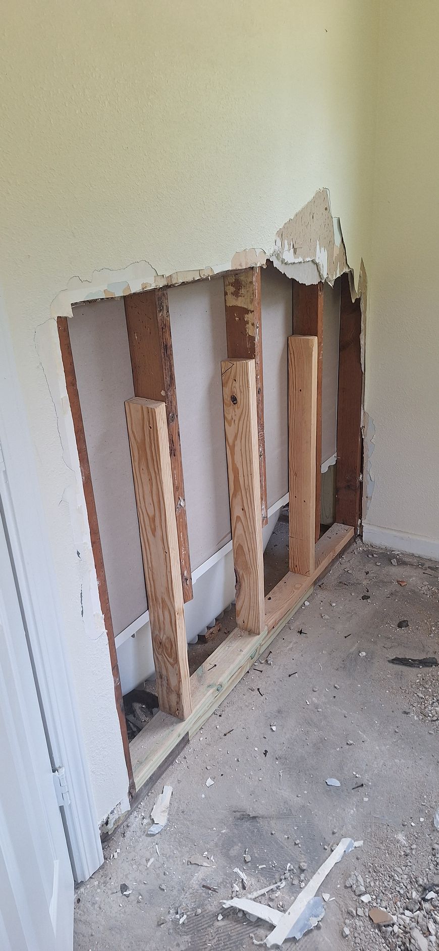 Damaged drywall exposing studs in a room corner, with debris on the floor.