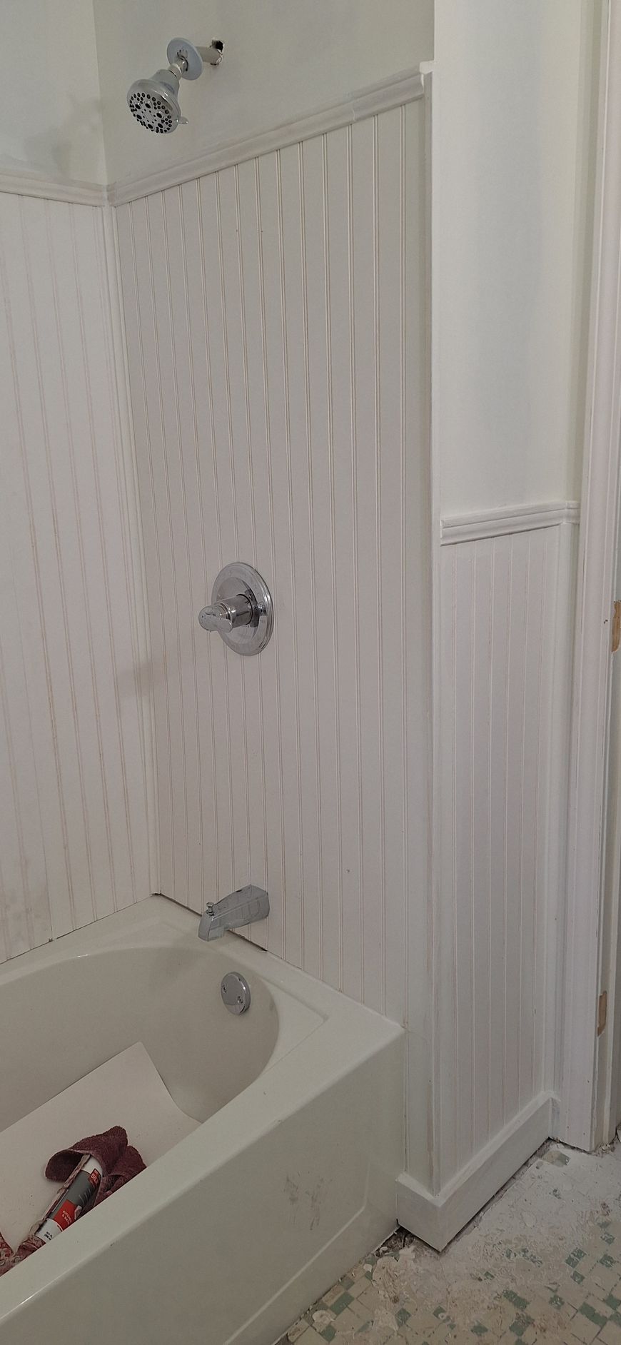 White bathroom with clawfoot tub, wall-mounted shower, and narrow beadboard paneling.