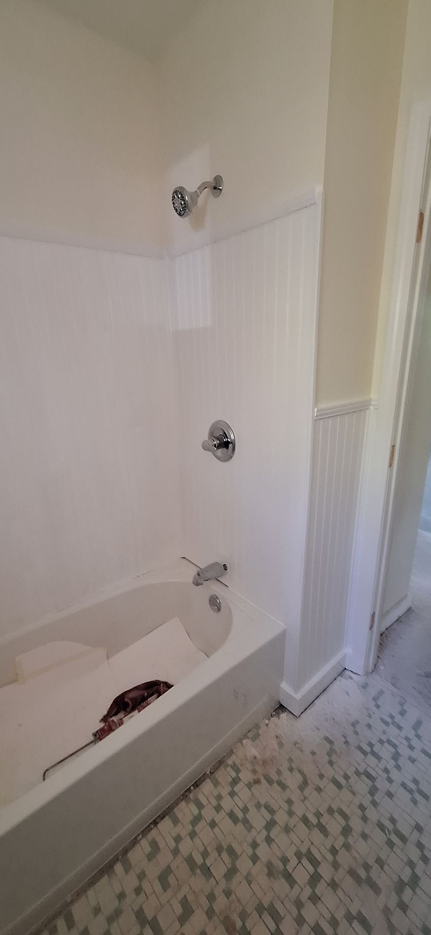 Small bathroom with white tub, tiled walls, exposed plumbing, and patterned floor.