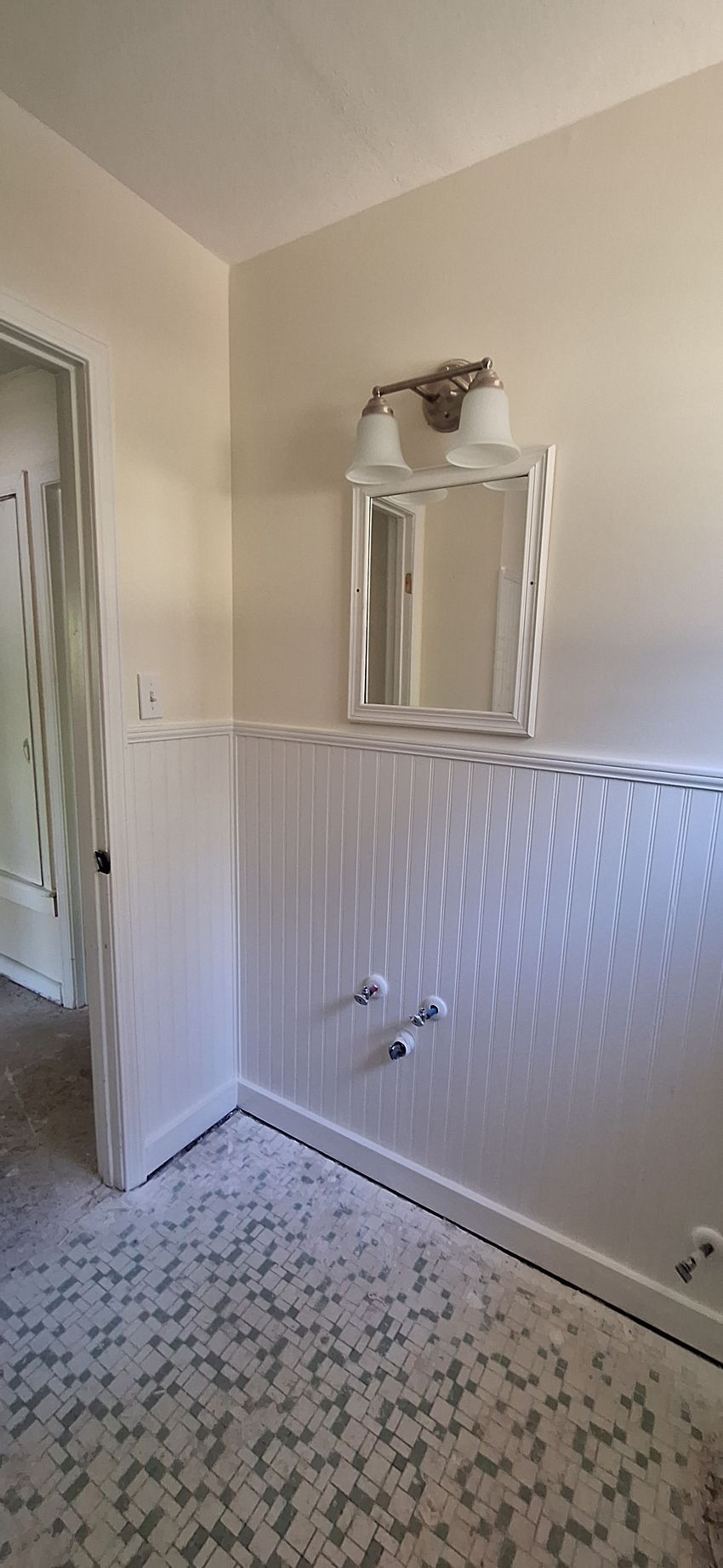 Small bathroom with a pedestal sink, mirror, towel ring, and patterned tile floor and wall tile.