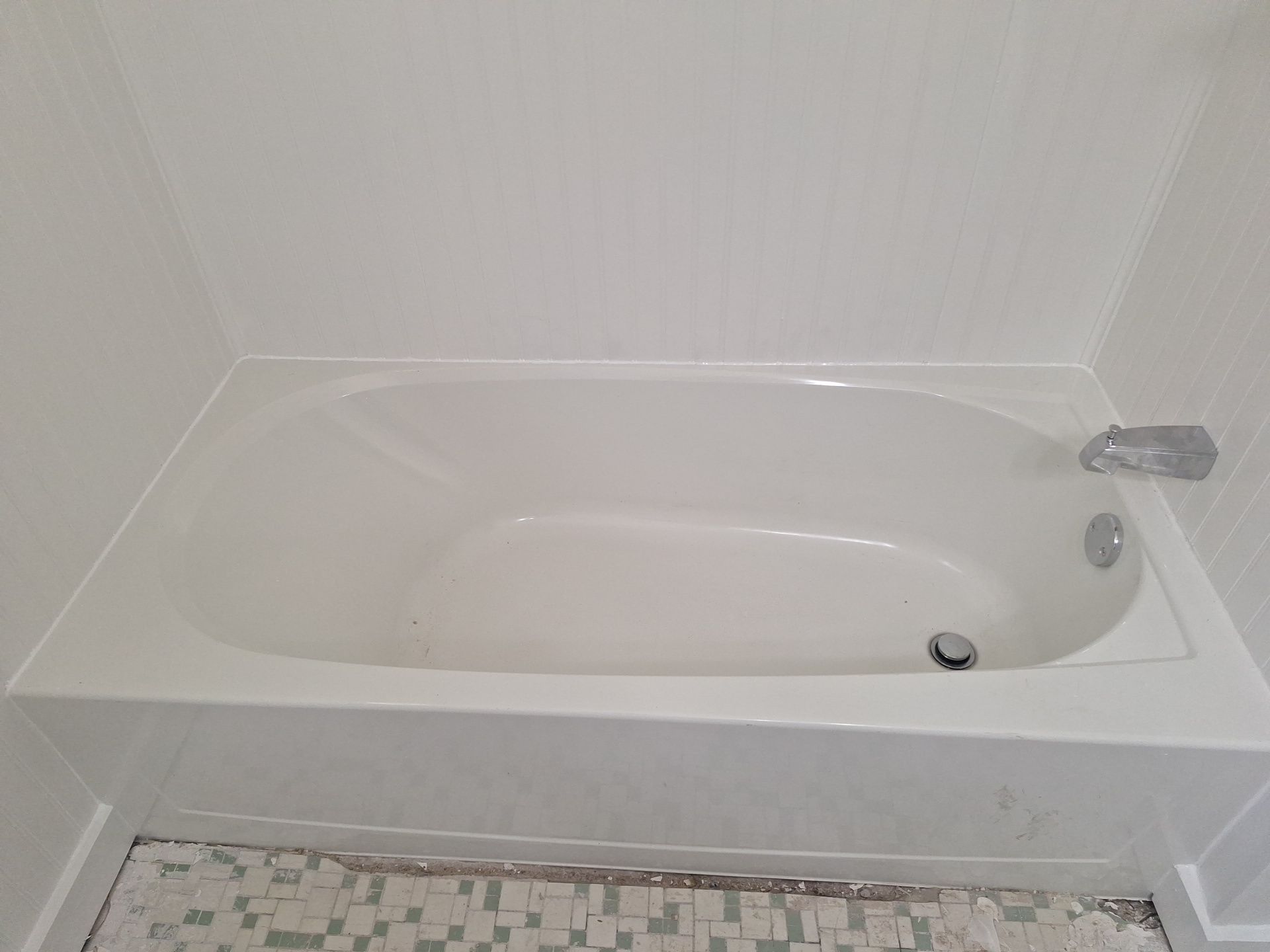 White bathtub with built-in seat and handheld shower in a tiled bathroom.