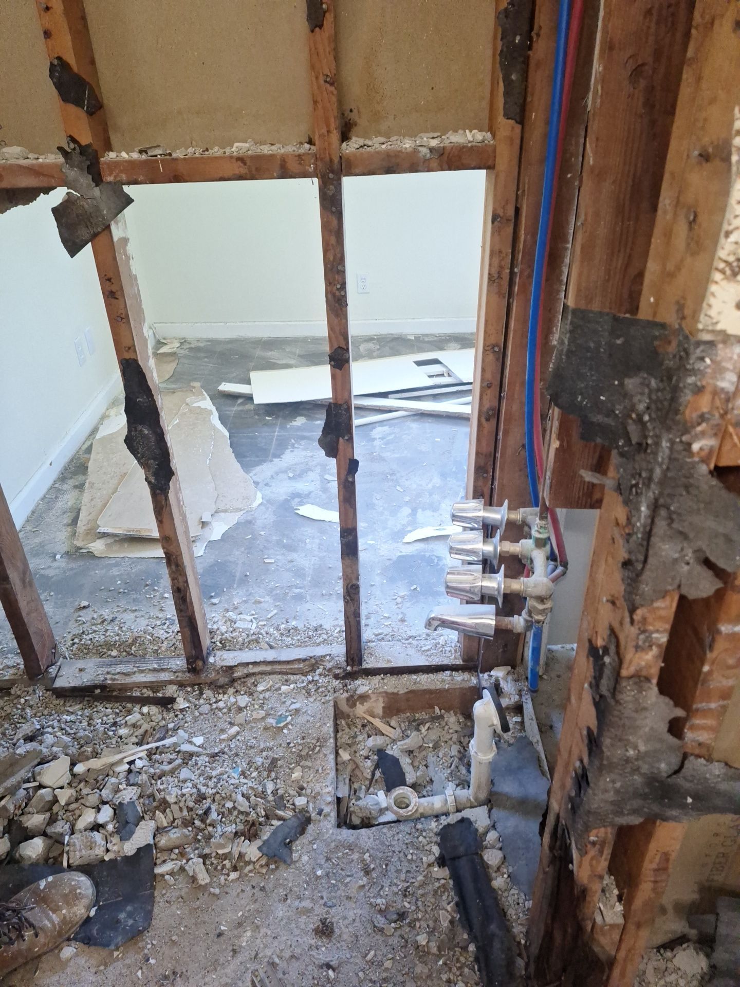 Damaged interior wall with exposed studs, debris on floor, and plumbing visible during renovation