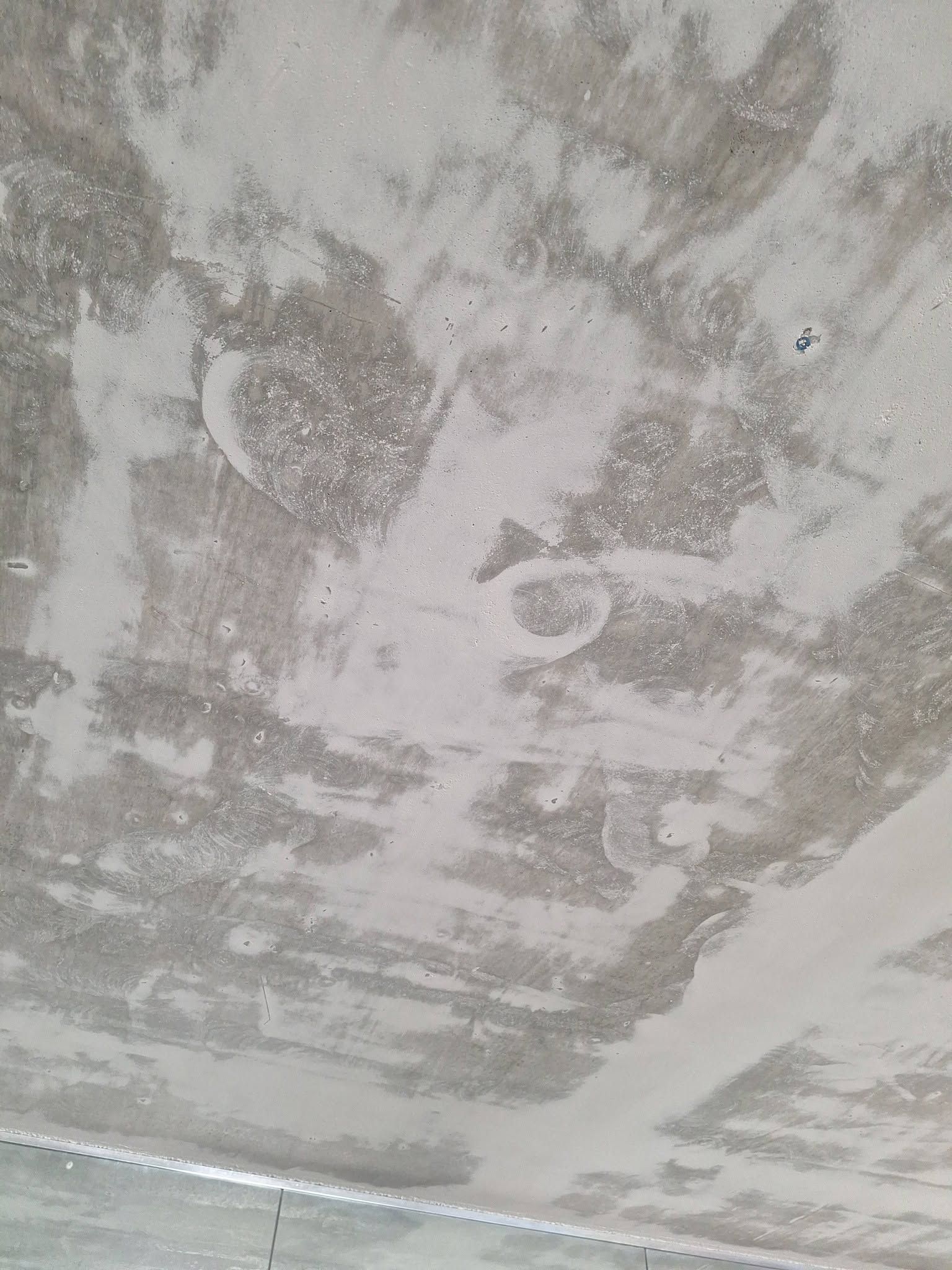 Peeling gray concrete ceiling with patches of exposed plaster and water damage