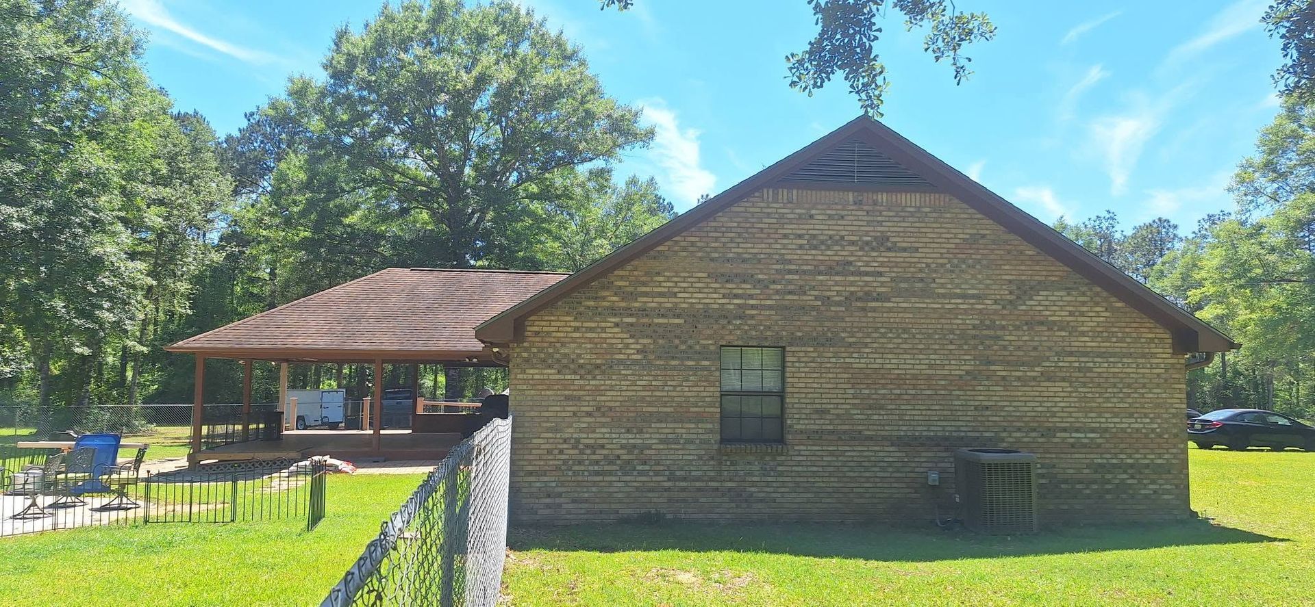 Historic log cabin and pavilion on a sunny green lawn with trees and a stone fence