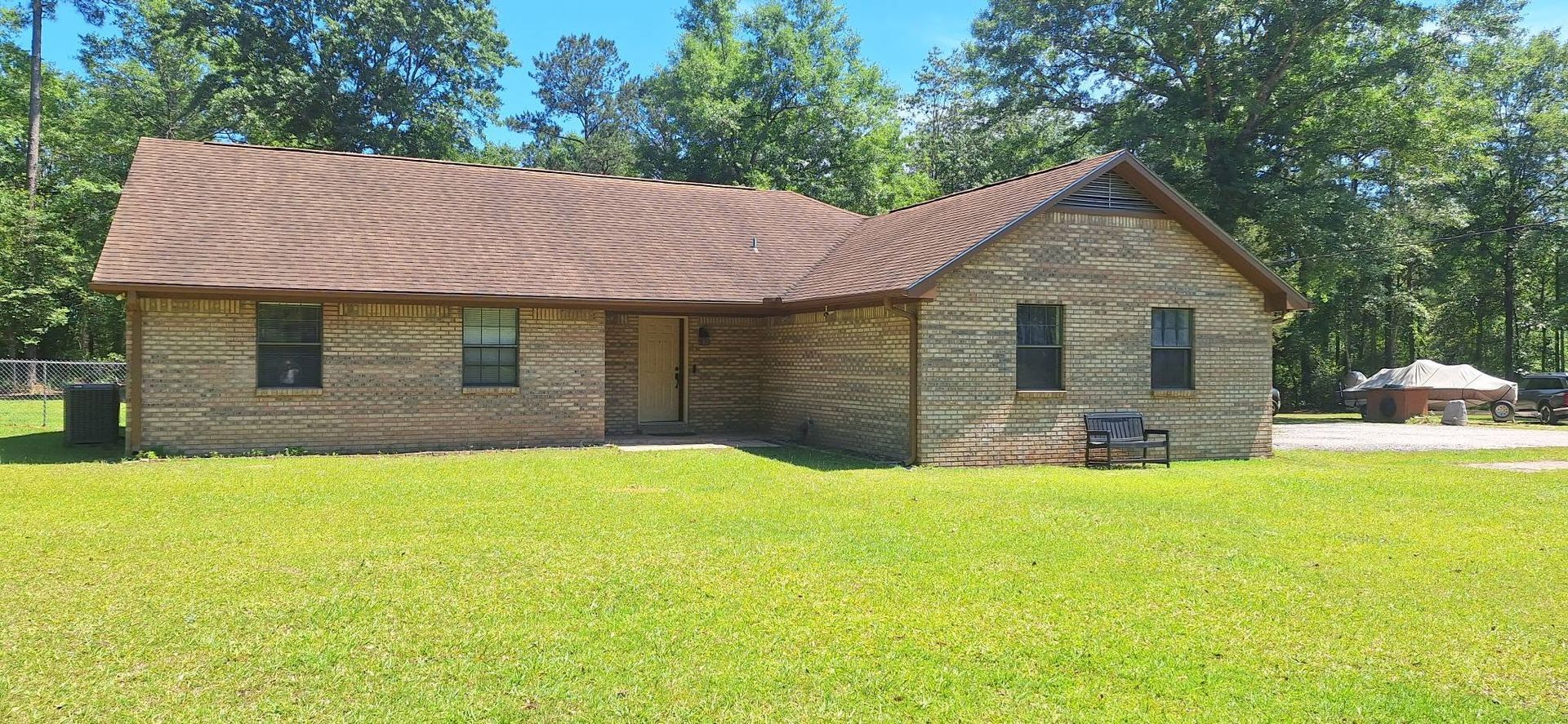 Single-story brick house with a wavy roof, set in a sunny grassy yard with trees behind it.