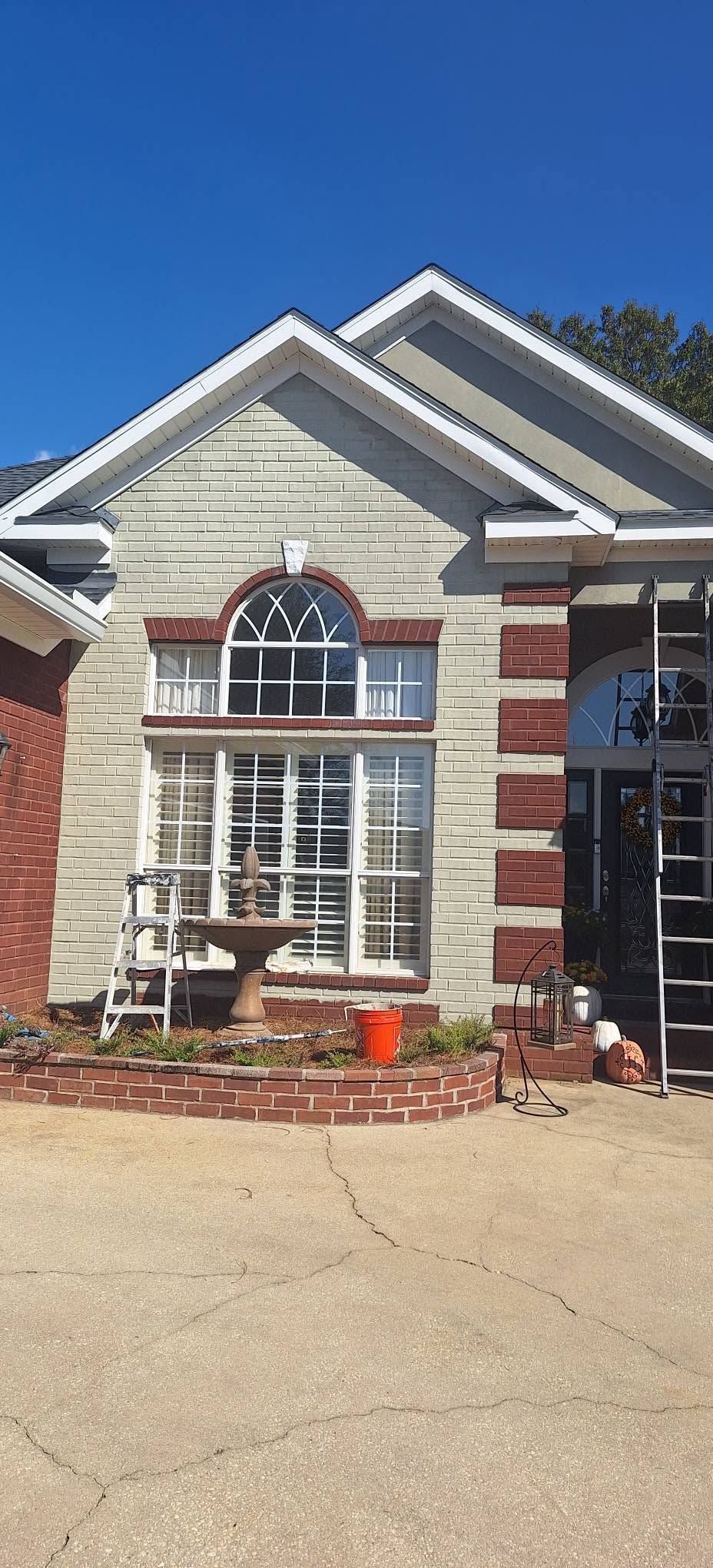 Front of a brick house with white trim, arched window, and a small patio table on a sunny day