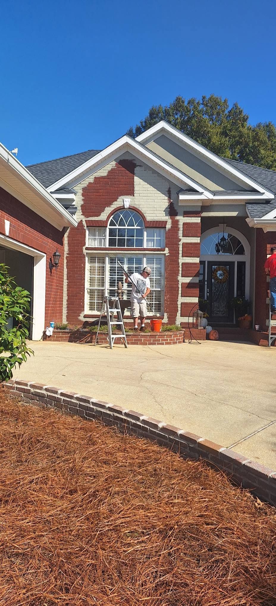 Brick house with arched front door, white trim, and a concrete driveway in bright sunlight