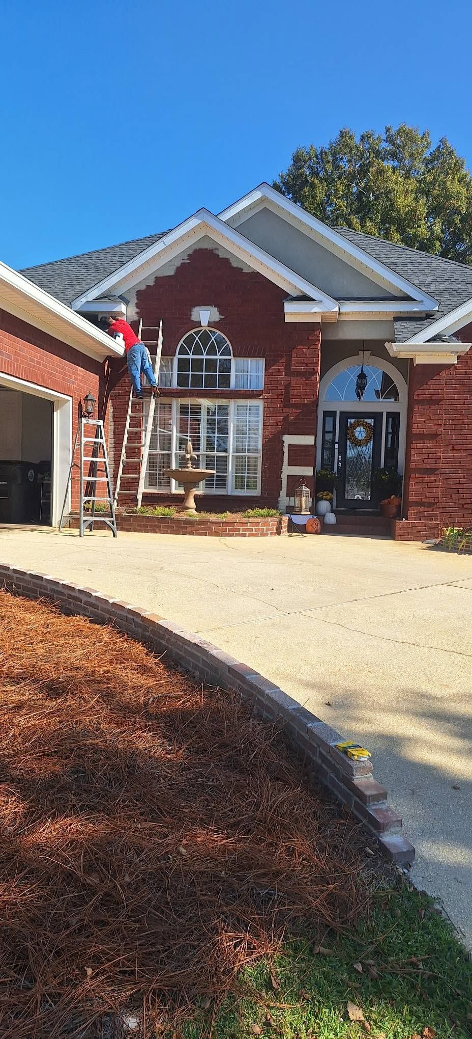 Brick house exterior with white trim, arched front door, and a worker on a ladder by the porch