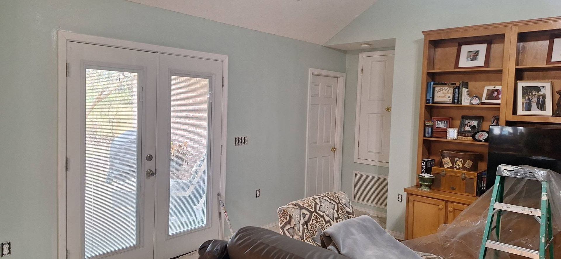 Bright living room with French doors, pale blue walls, sofa, and wooden bookshelf.