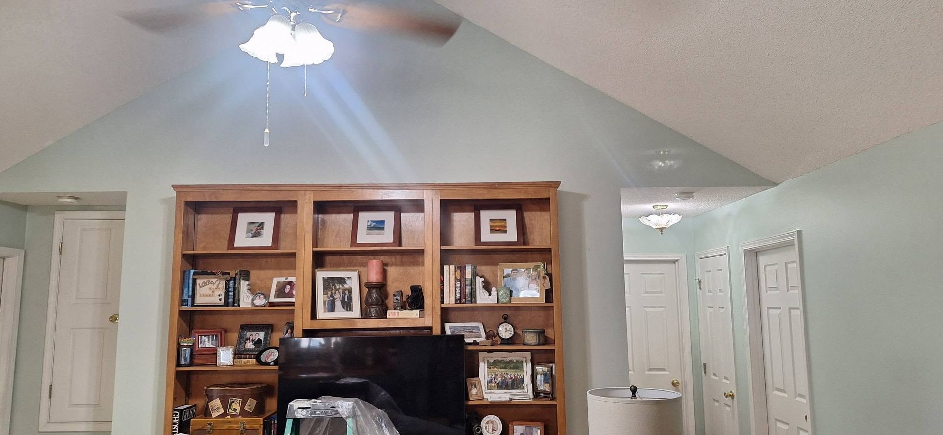 Living room with vaulted ceiling, ceiling fan, and built-in wooden shelves around a TV fireplace