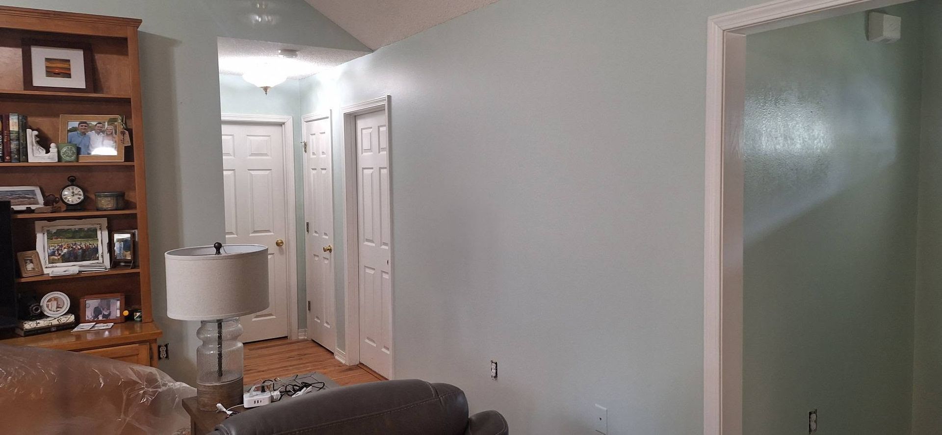 Living room hallway with white doors, a lamp, and a wooden shelf against pale walls