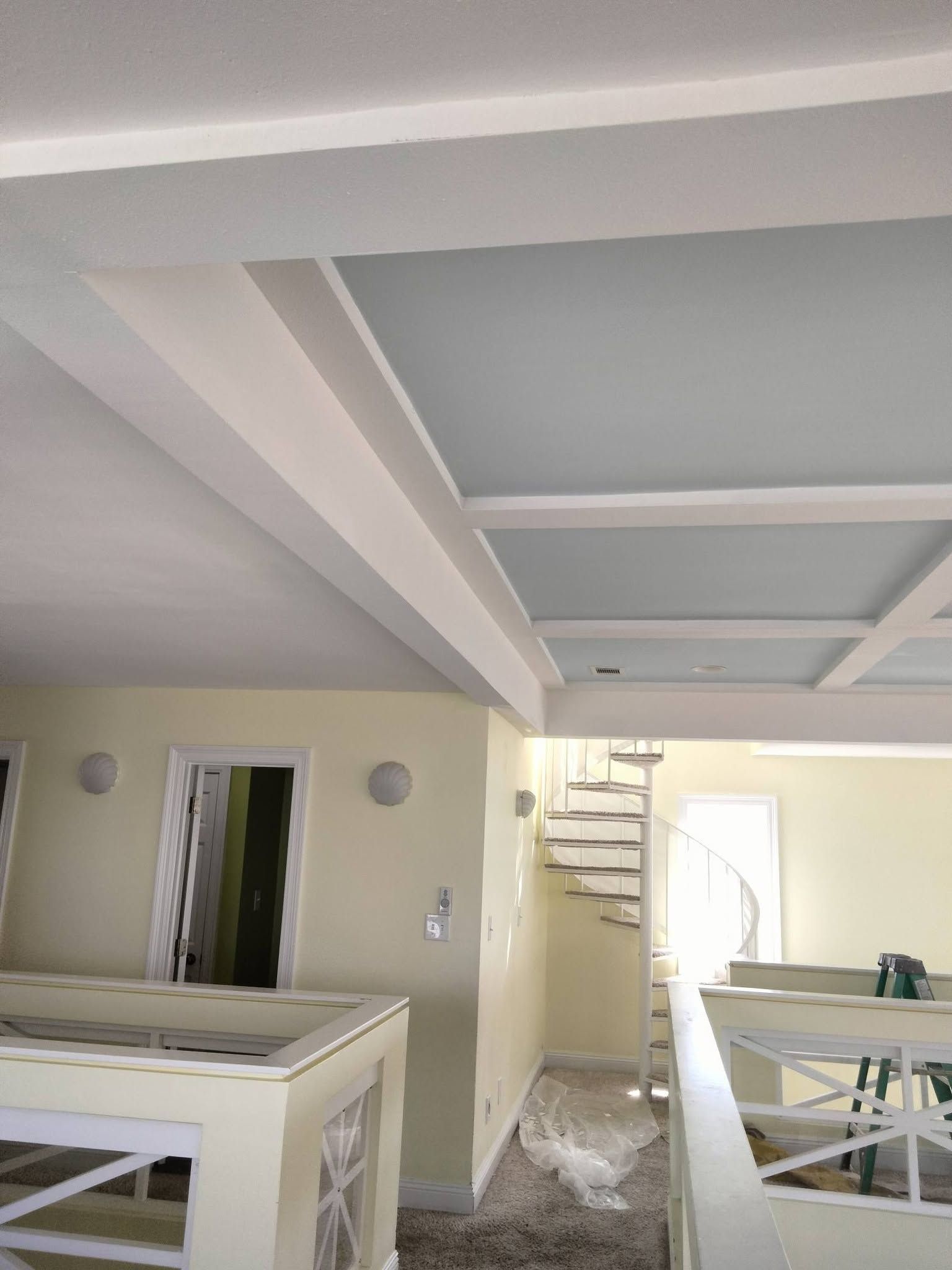 Partially renovated room with drywall ceiling, beige walls, and a staircase visible in the background