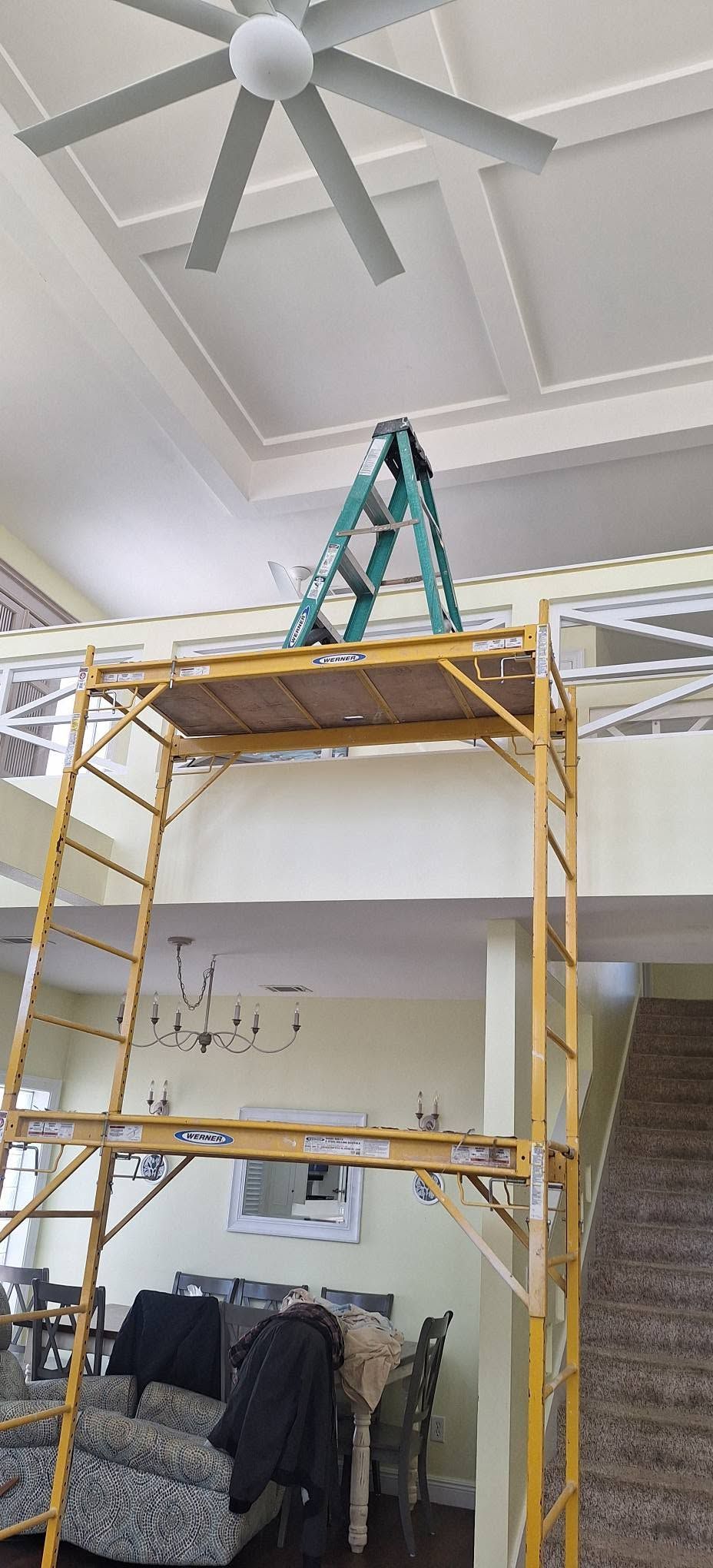 Yellow scaffold with teal ladder in a high-ceiling room beneath a ceiling fan