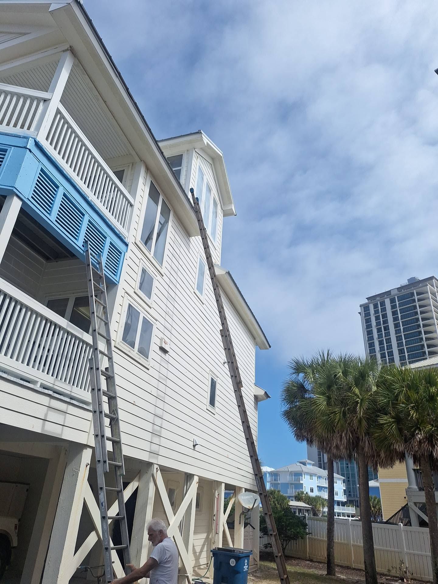 White stilted building with blue balconies beside palm trees under a cloudy sky
