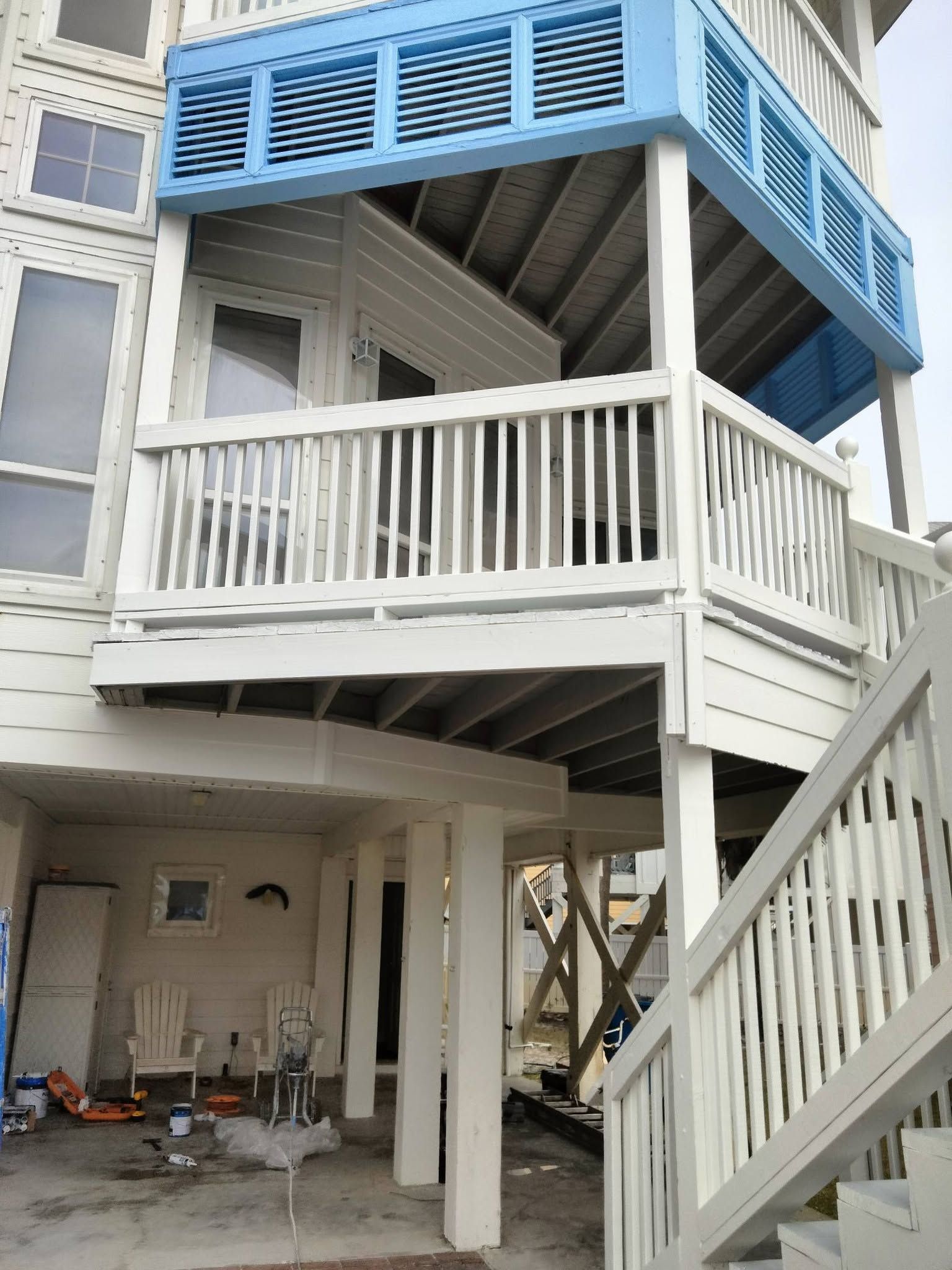 Stilt house with white railings and blue shutters, showing stairway and undercroft area under renovation