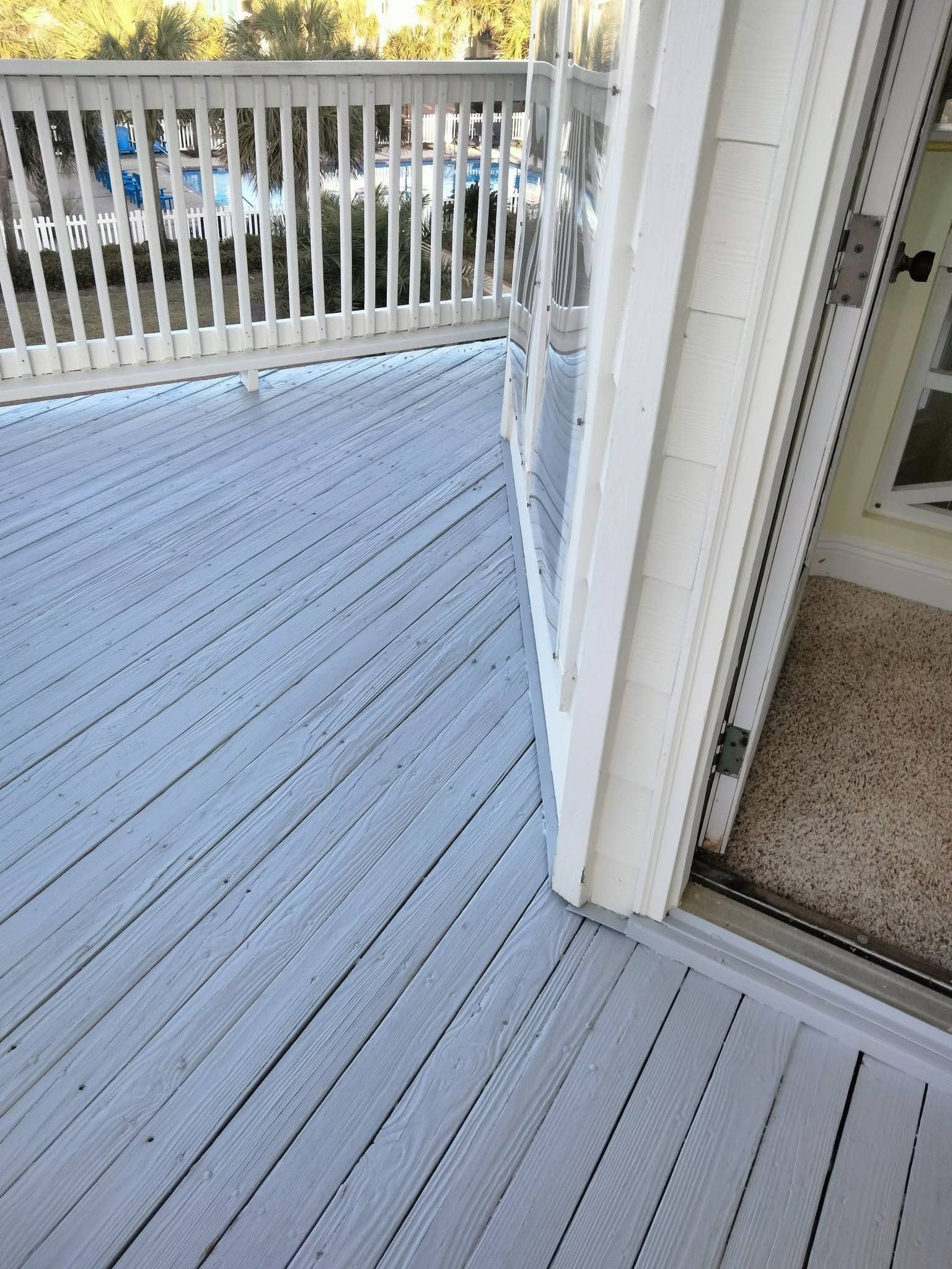 Light gray deck with white railing beside a sliding glass door, overlooking parked cars.