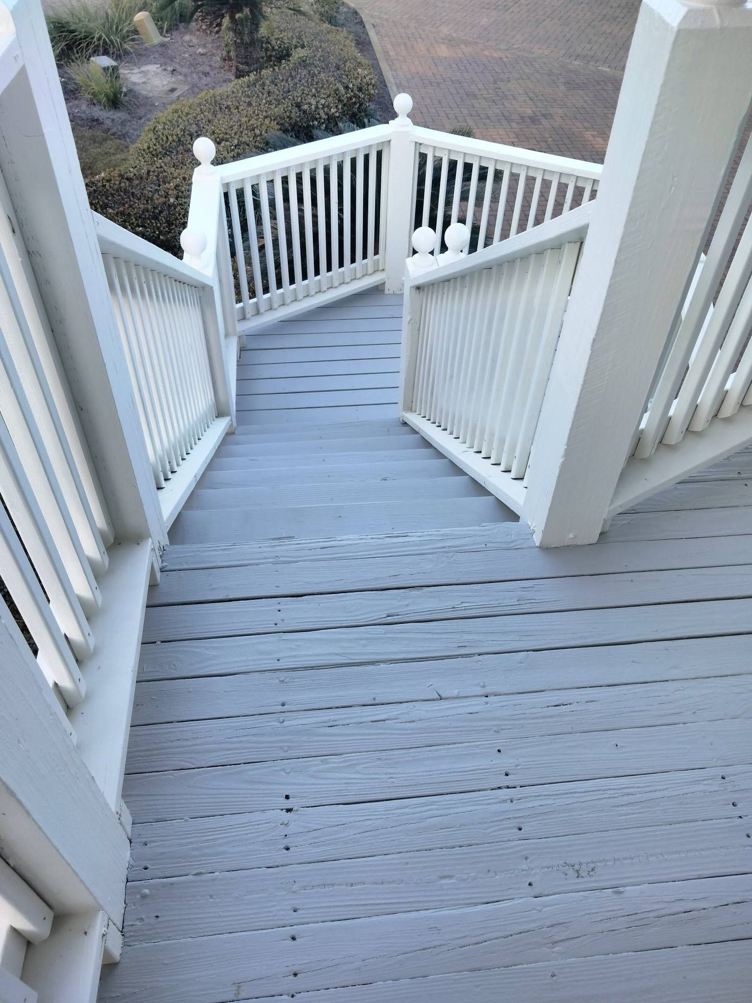 Steep gray wooden stairs with white railings leading down to a landscaped yard
