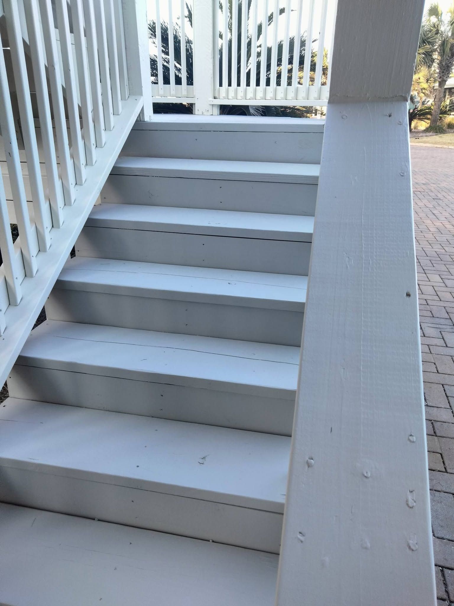 White wooden stairs and railing on a porch beside a paved walkway.