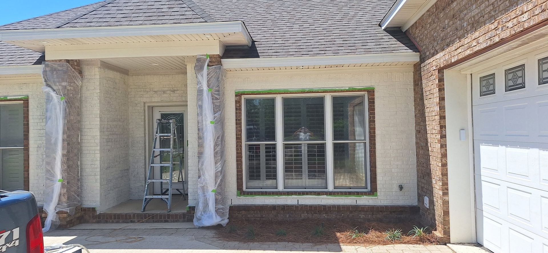 Front of a brick house with a covered porch, large window, and white garage door.