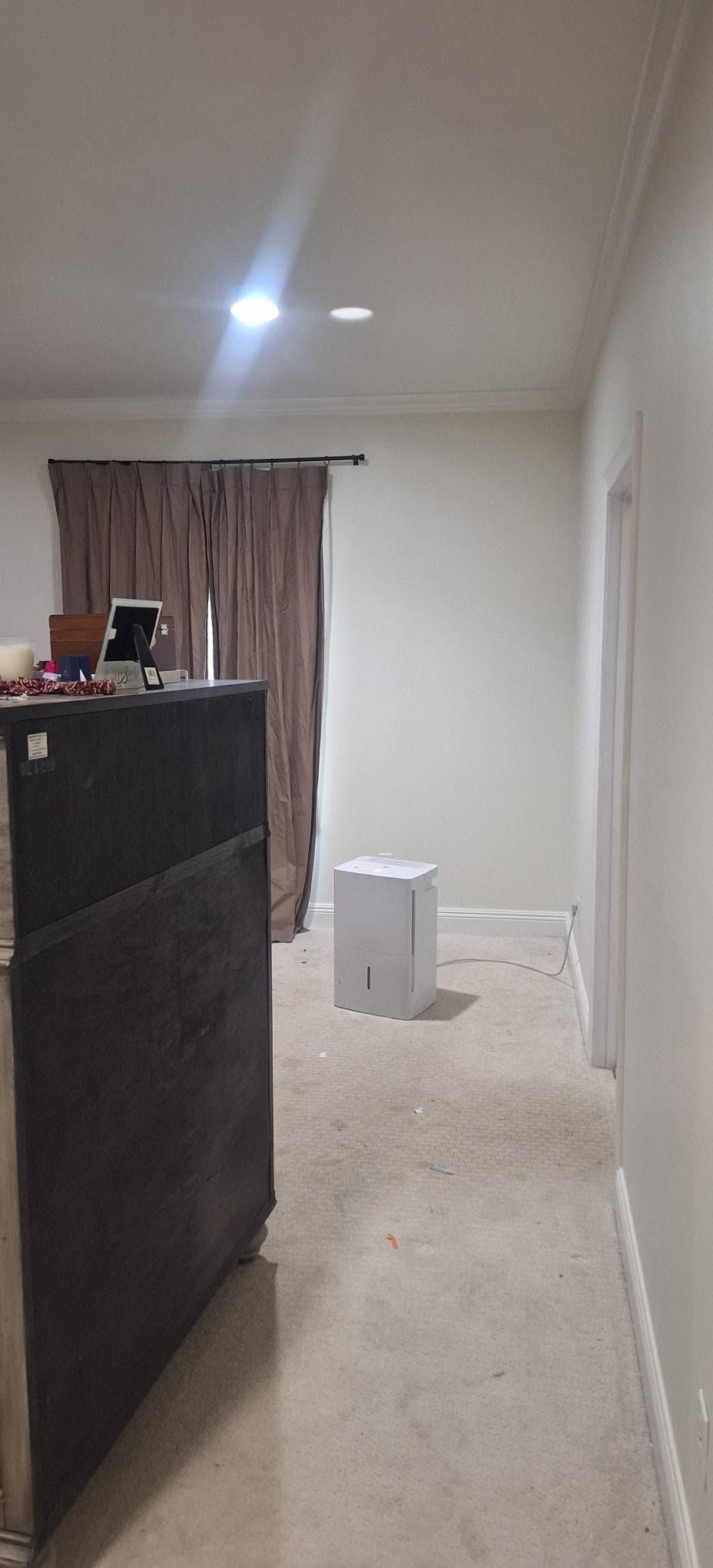 Narrow empty hallway with white walls, a dark cabinet on the left, and a small stool near the back.