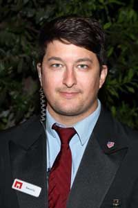A man wearing a suit and tie is standing in front of a tree.