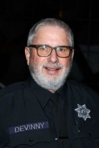 A man with a beard and glasses is wearing a name tag that says devinny.