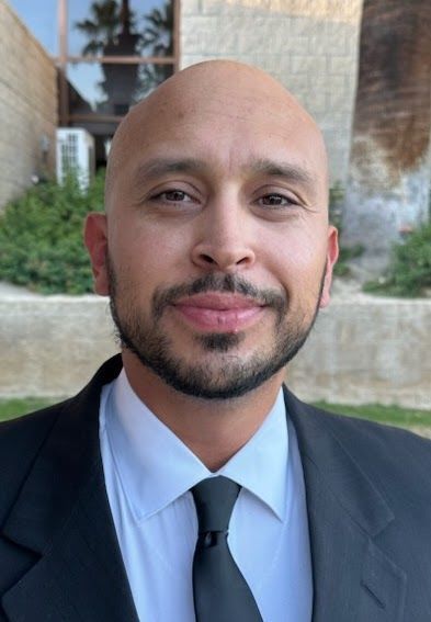 A bald man with a beard is wearing a suit and tie.