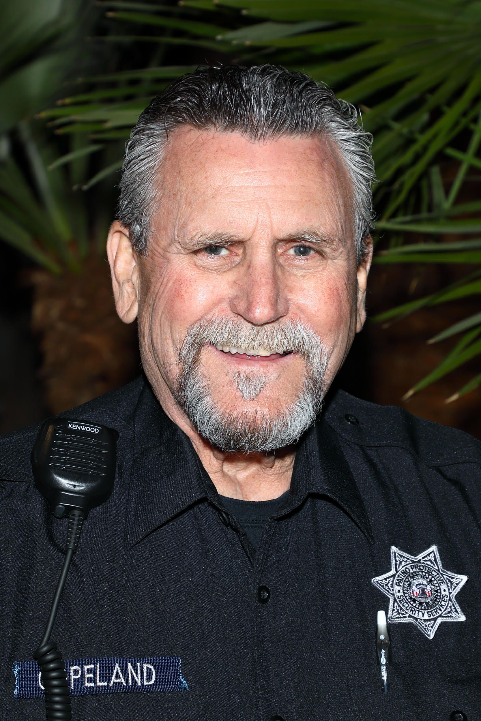 A man with a beard is wearing a police uniform and smiling.