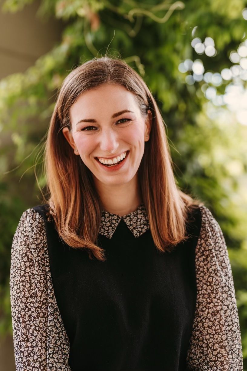 A woman wearing a black vest and a floral shirt is smiling for the camera.