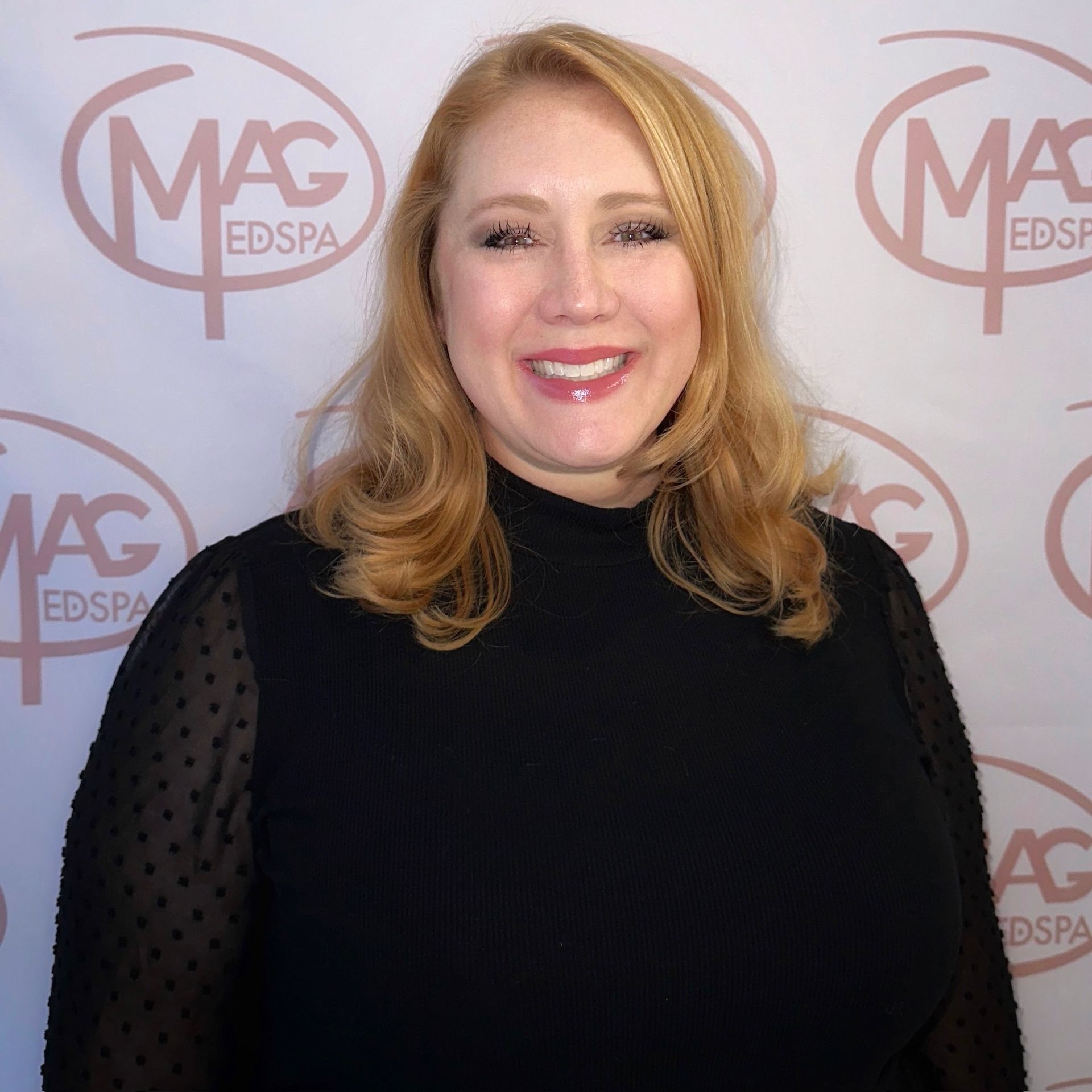 A woman wearing a necklace and hoop earrings smiles for the camera