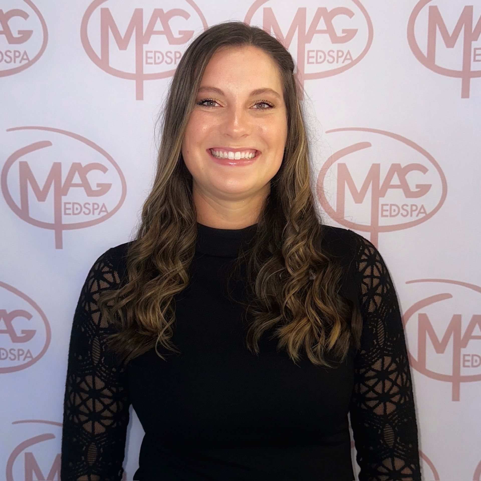 A woman wearing a necklace and hoop earrings smiles for the camera