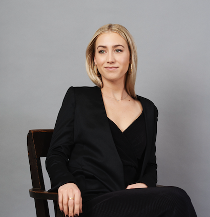 A woman in a black suit is sitting in a chair
