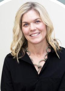 A woman wearing a black shirt and a necklace is smiling for the camera.