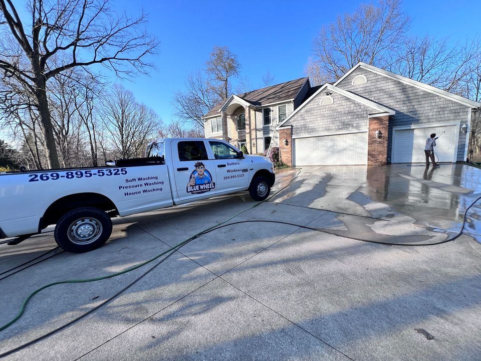 White service truck in driveway outside a house, with a worker washing the garage and driveway with a pressure washer.