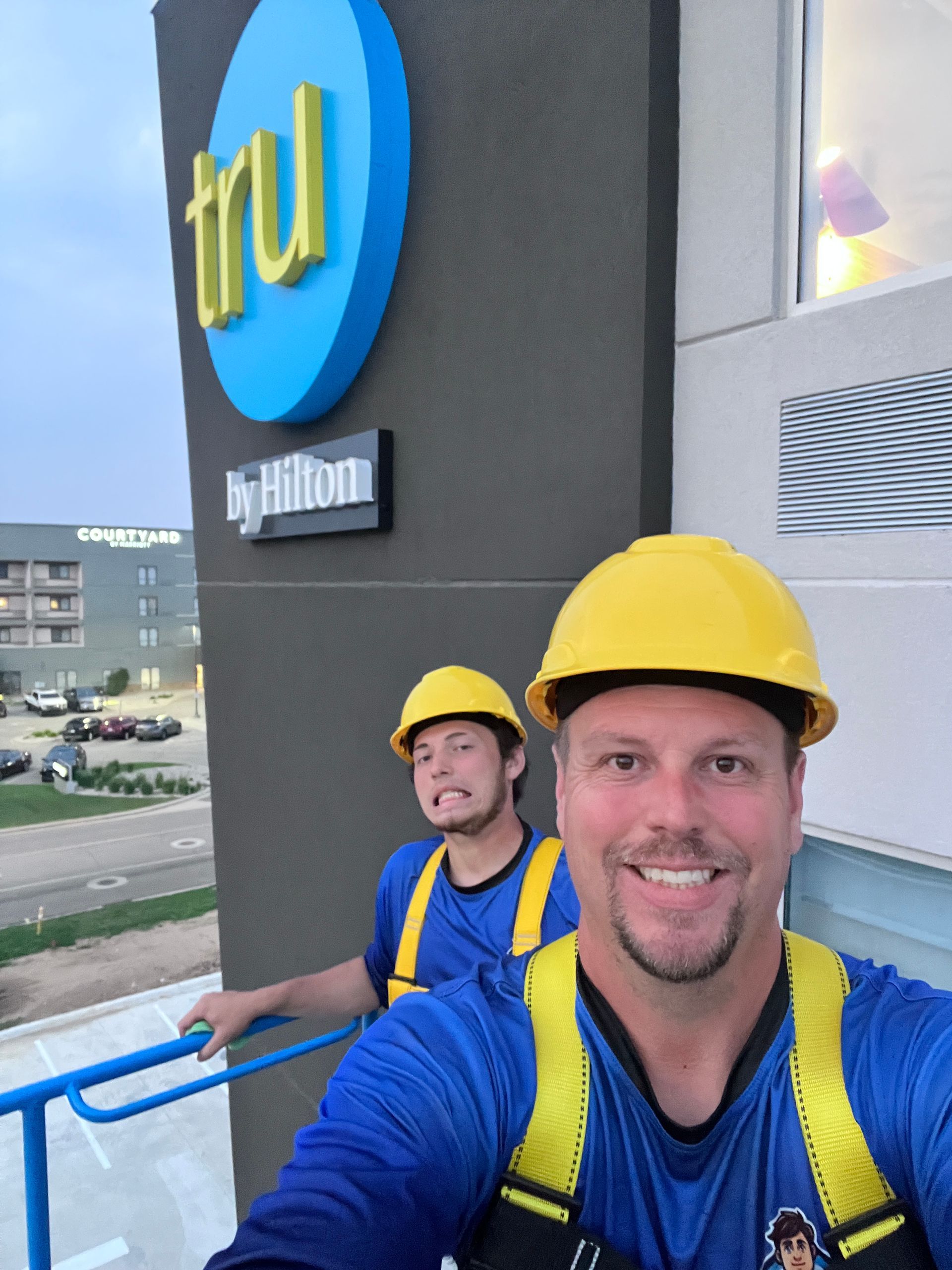 Two workers in yellow hard hats on a platform outside a Fruition building sign
