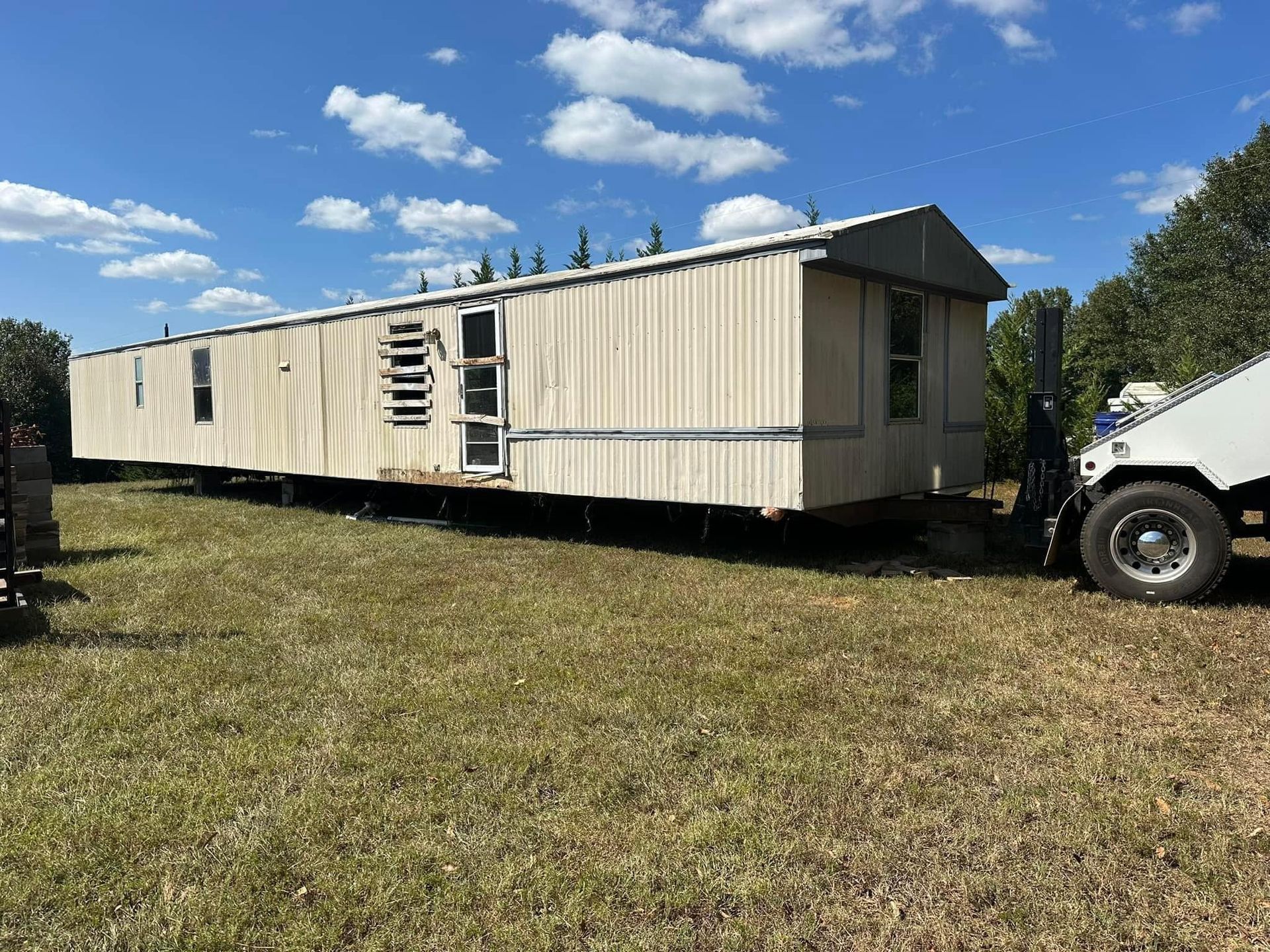 A mobile home is being towed by a forklift in a grassy field.