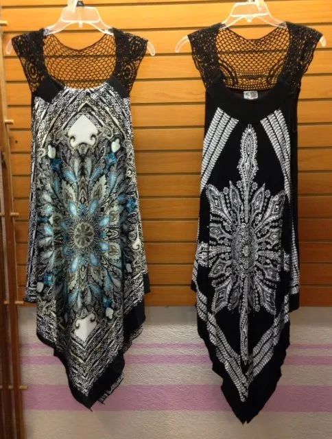 Two patterned sleeveless dresses hanging on hangers, one blue and one black, against a wooden wall.