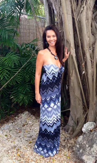 Woman in a blue zigzag dress standing beside a tree in a tropical garden