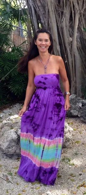 Woman standing outdoors in a purple strapless dress with a colorful striped hem.