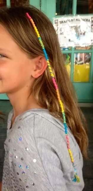 Profile of a child with long brown hair and colorful braided strands in a classroom setting